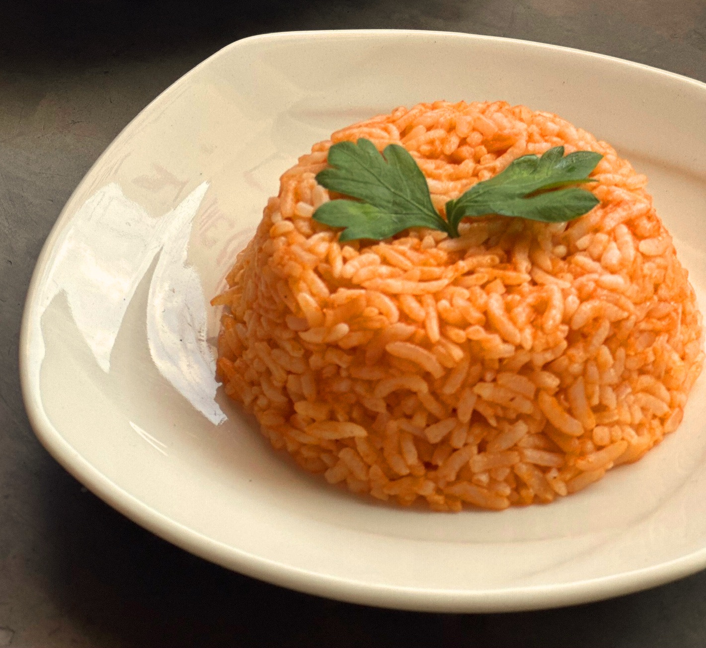 Overhead shot of arroz rojo in a white plate, scattered with fresh parsley.