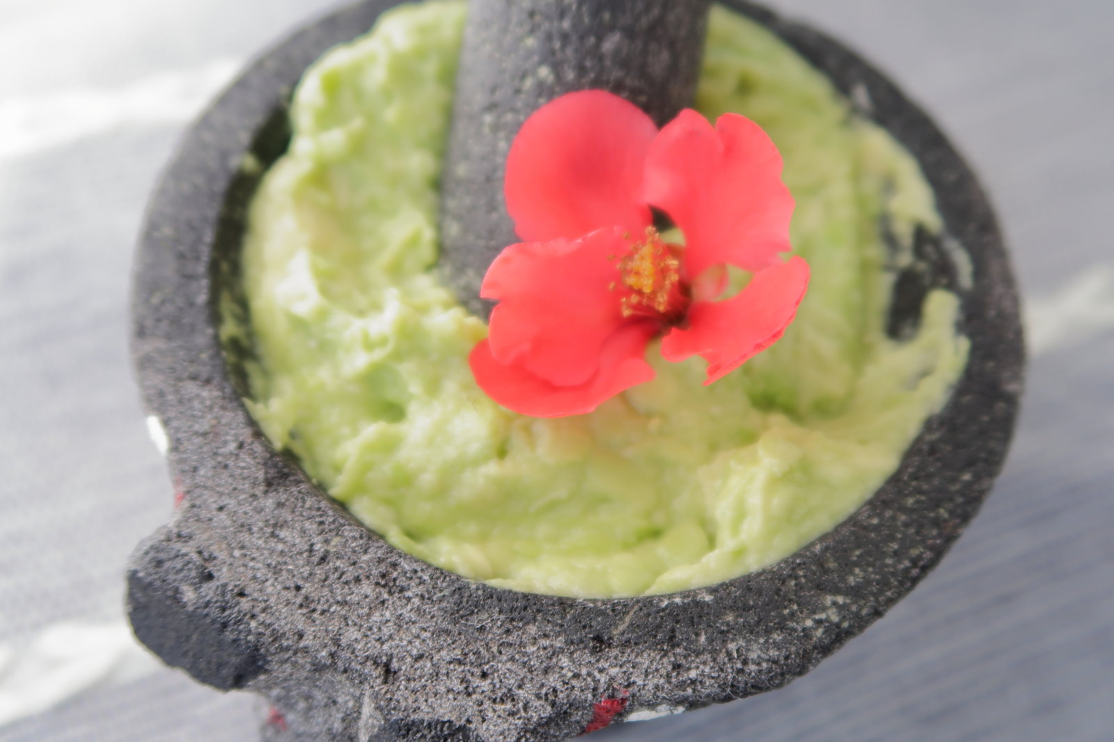 Overhead shot of vivid green guacamole in a black volcanic stone molcajete, garnished with a single red flower.